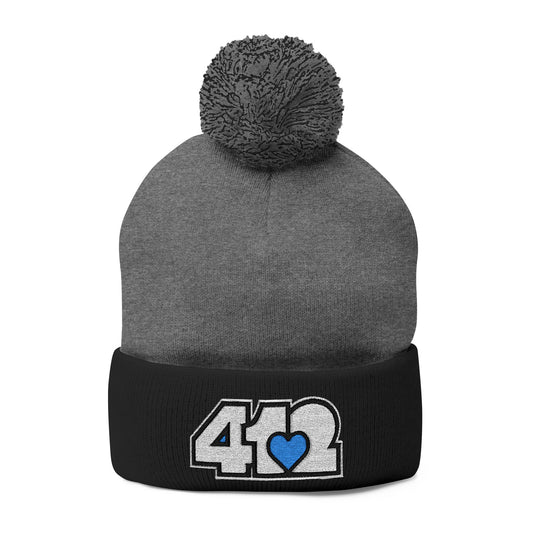 Cozy 412 Tossle Cap | Embroidered White and Blue Logo. Apparel Color: Dark Heather Grey / Black. Has soft acrylic knit, fold-over cuff, and one-size fit for winter comfort.