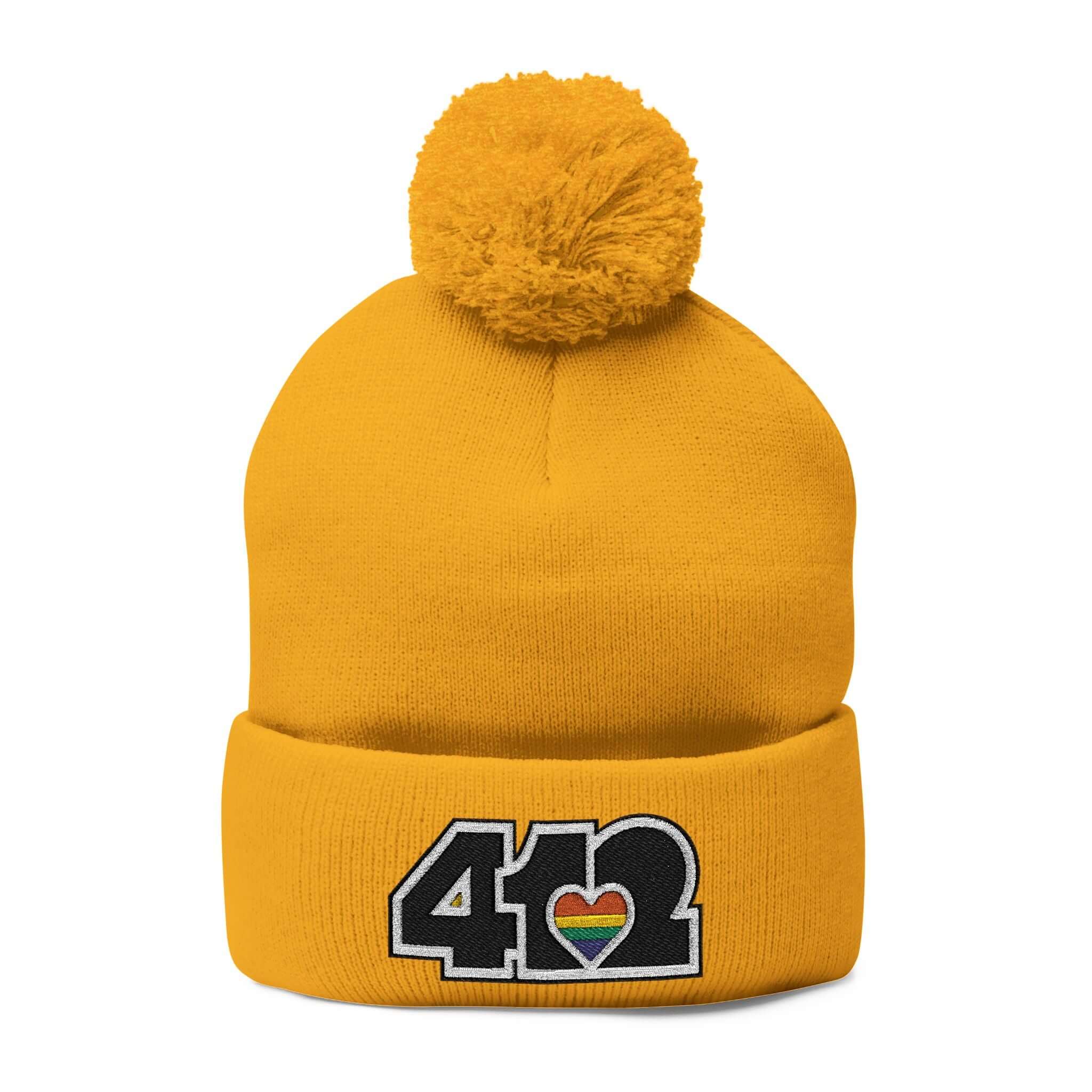 Cozy 412 Tossle Cap | Embroidered Black and Rainbow Logo. Apparel Color: Gold. Has soft acrylic knit, fold-over cuff, and one-size fit for winter comfort.