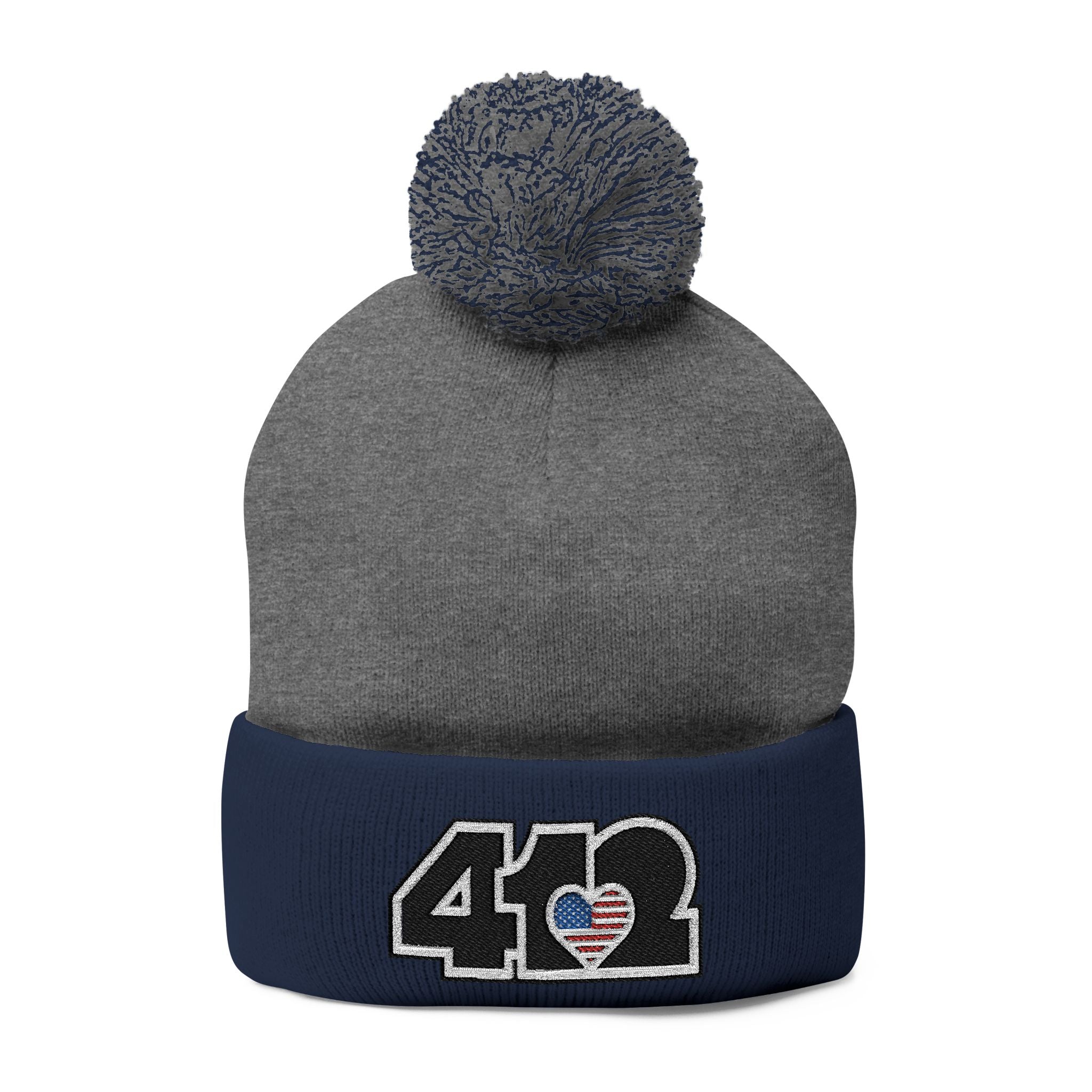 412 Tossle Cap | Embroidered Stars & Stripes Black Logo. Apparel Color: Dark Heather Grey / Navy. Has soft acrylic knit, fold-over cuff, and one-size fit for winter comfort.