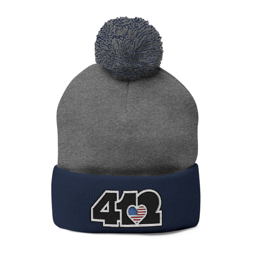 412 Tossle Cap | Embroidered Stars & Stripes Black Logo. Apparel Color: Dark Heather Grey / Navy. Has soft acrylic knit, fold-over cuff, and one-size fit for winter comfort.