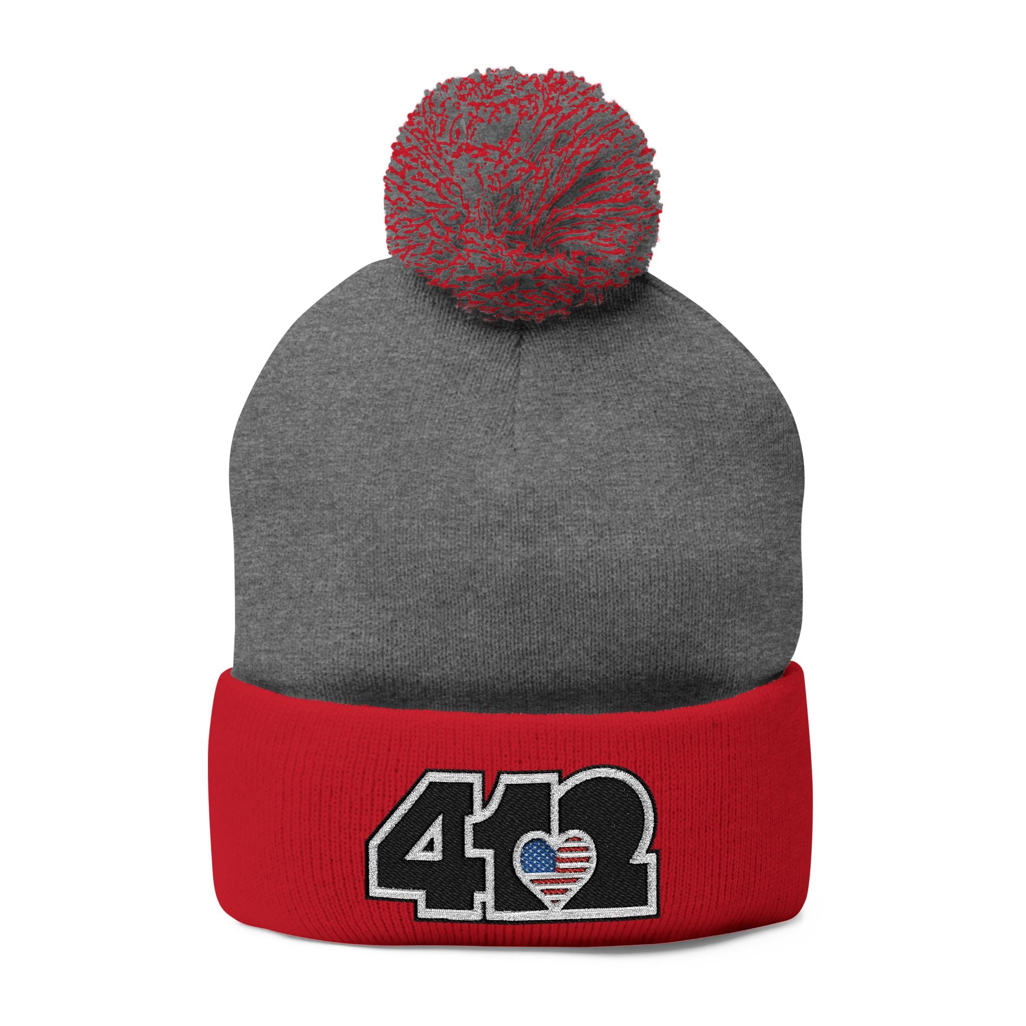 412 Tossle Cap | Embroidered Stars & Stripes Black Logo. Apparel Color: Dark Heather Grey / Red. Has soft acrylic knit, fold-over cuff, and one-size fit for winter comfort.