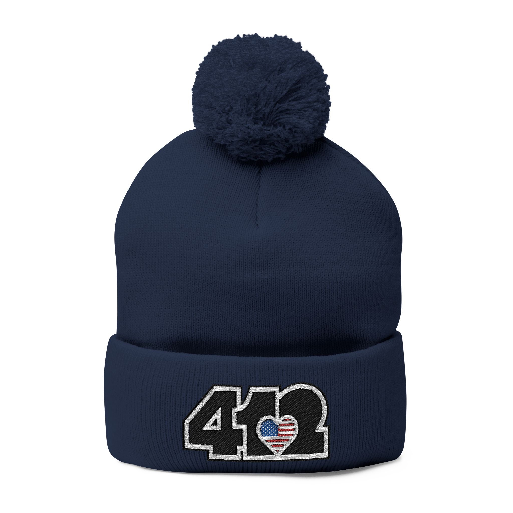 412 Tossle Cap | Embroidered Stars & Stripes Black Logo. Apparel Color: Navy. Has soft acrylic knit, fold-over cuff, and one-size fit for winter comfort.