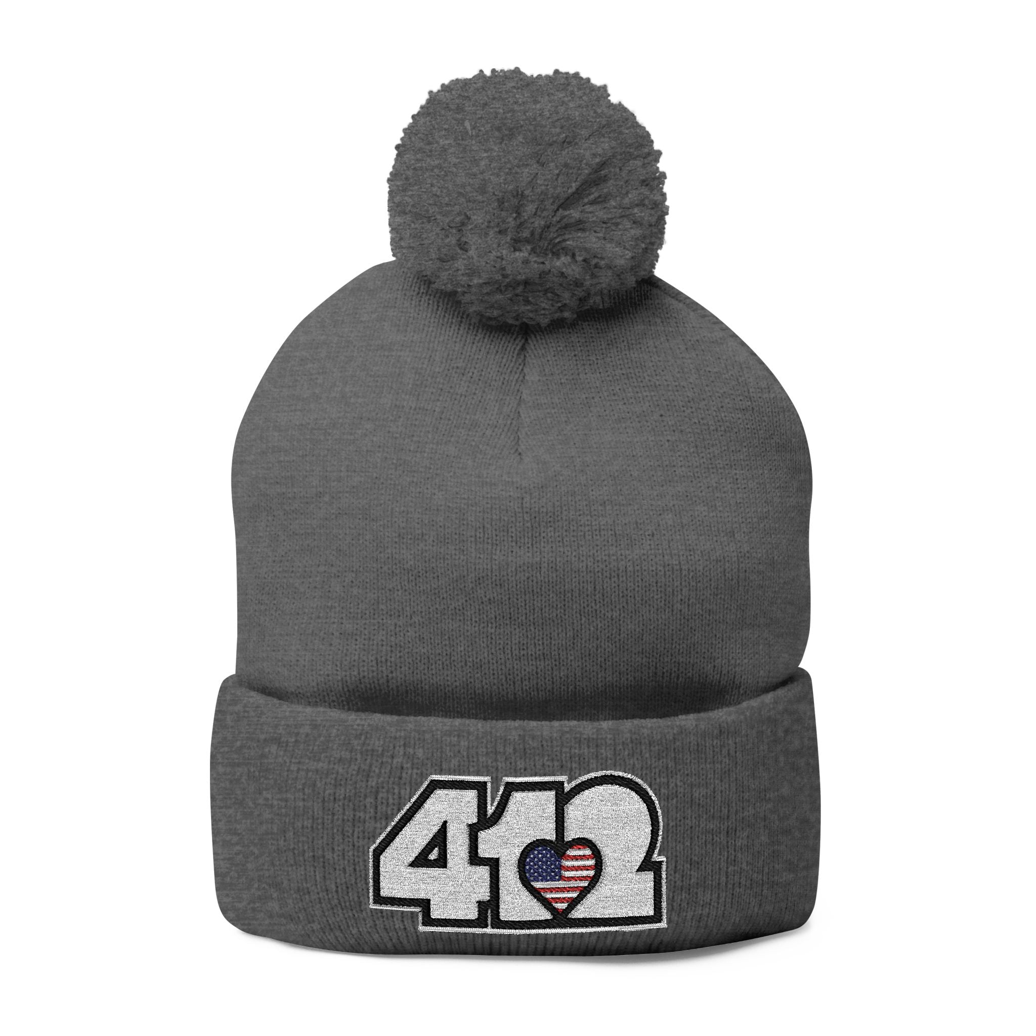 412 Tossle Cap | Embroidered Stars & Stripes White Logo. Apparel Color: Dark Heather Grey. Has soft acrylic knit, fold-over cuff, and one-size fit for winter comfort.