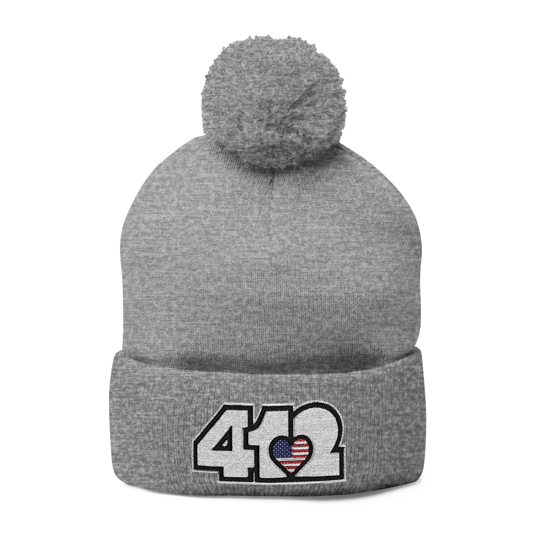412 Tossle Cap | Embroidered Stars & Stripes White Logo. Apparel Color: Heather Grey. Has soft acrylic knit, fold-over cuff, and one-size fit for winter comfort.