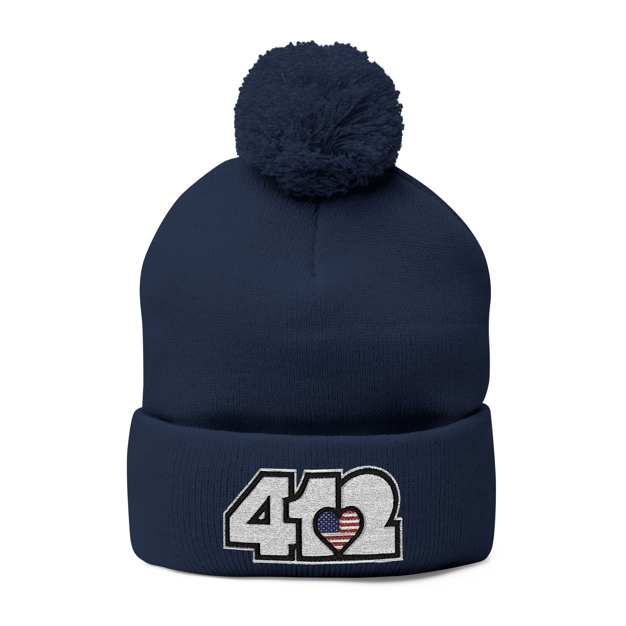 412 Tossle Cap | Embroidered Stars & Stripes White Logo. Apparel Color: Navy. Has soft acrylic knit, fold-over cuff, and one-size fit for winter comfort.