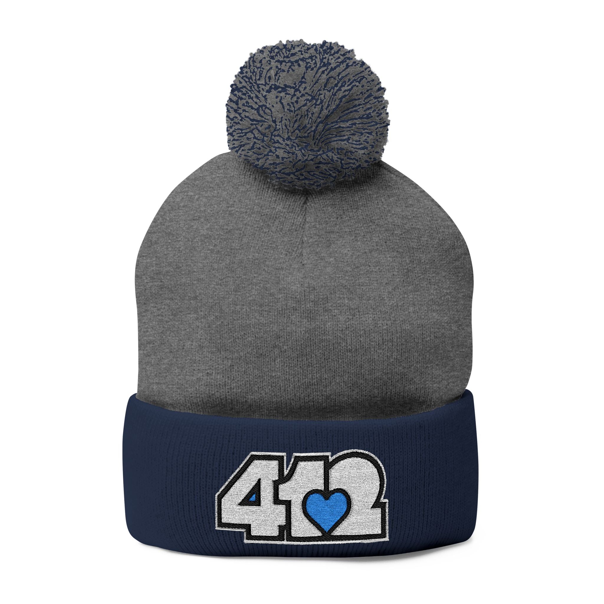 412 Tossle Cap | Embroidered White and Blue Logo. Apparel Color: Dark Heather Grey / Navy. Has soft acrylic knit, fold-over cuff, and one-size fit for winter comfort.