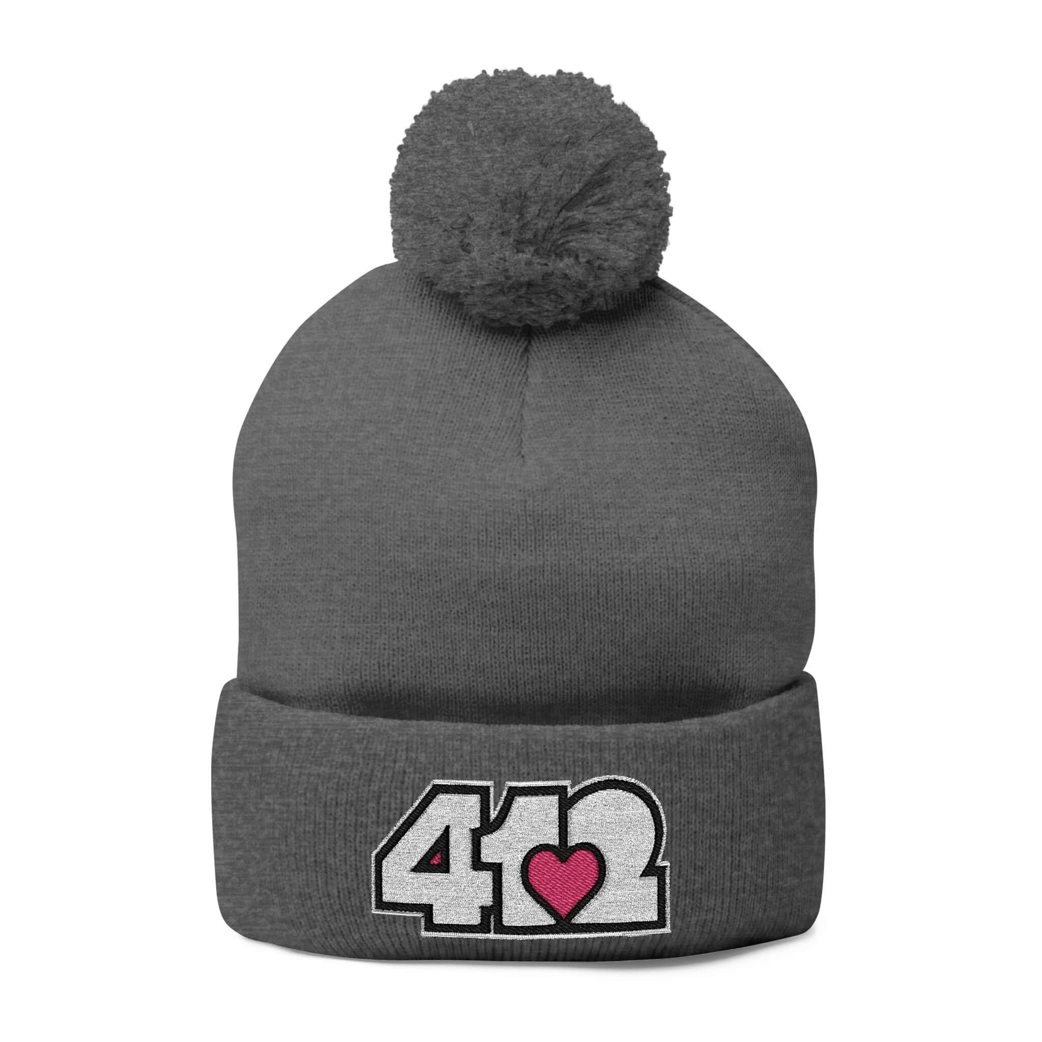 Cozy 412 Tossle Cap | Embroidered White and Pink Logo. Apparel Color: Dark Heather Grey. Has soft acrylic knit, fold-over cuff, and one-size fit for winter comfort.
